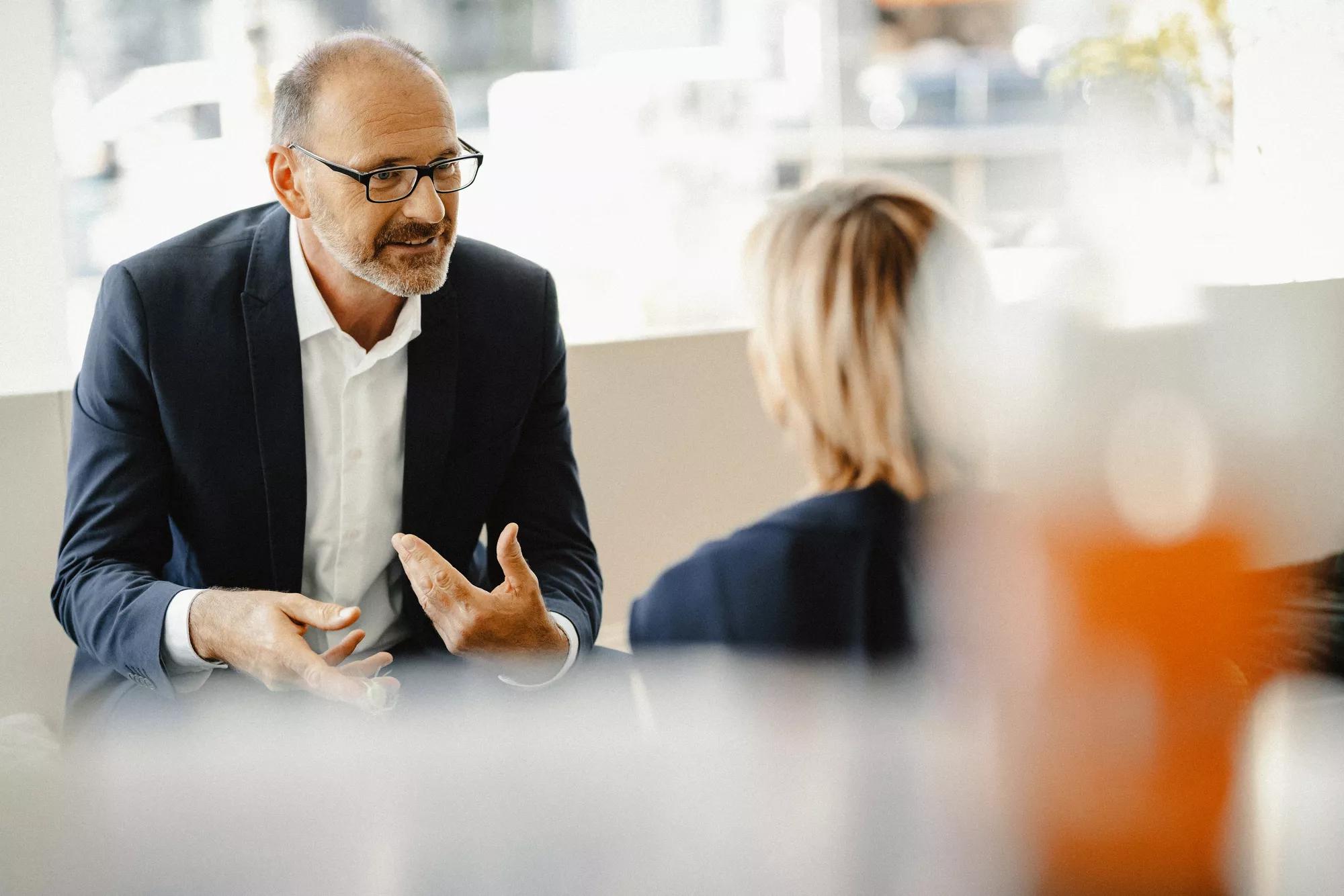 Portrait of bearded businessman in eyeglasses working with laptop while sitting in restaurant outdoors.