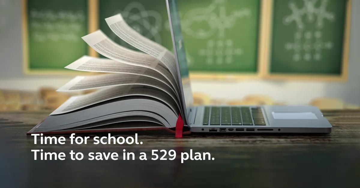 A book leaning against a laptop in front of a chalkboard.