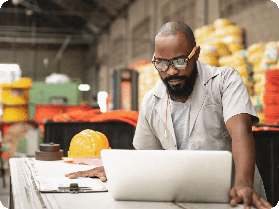 Business owner standing at a desk in a warehouse looking at a laptop.