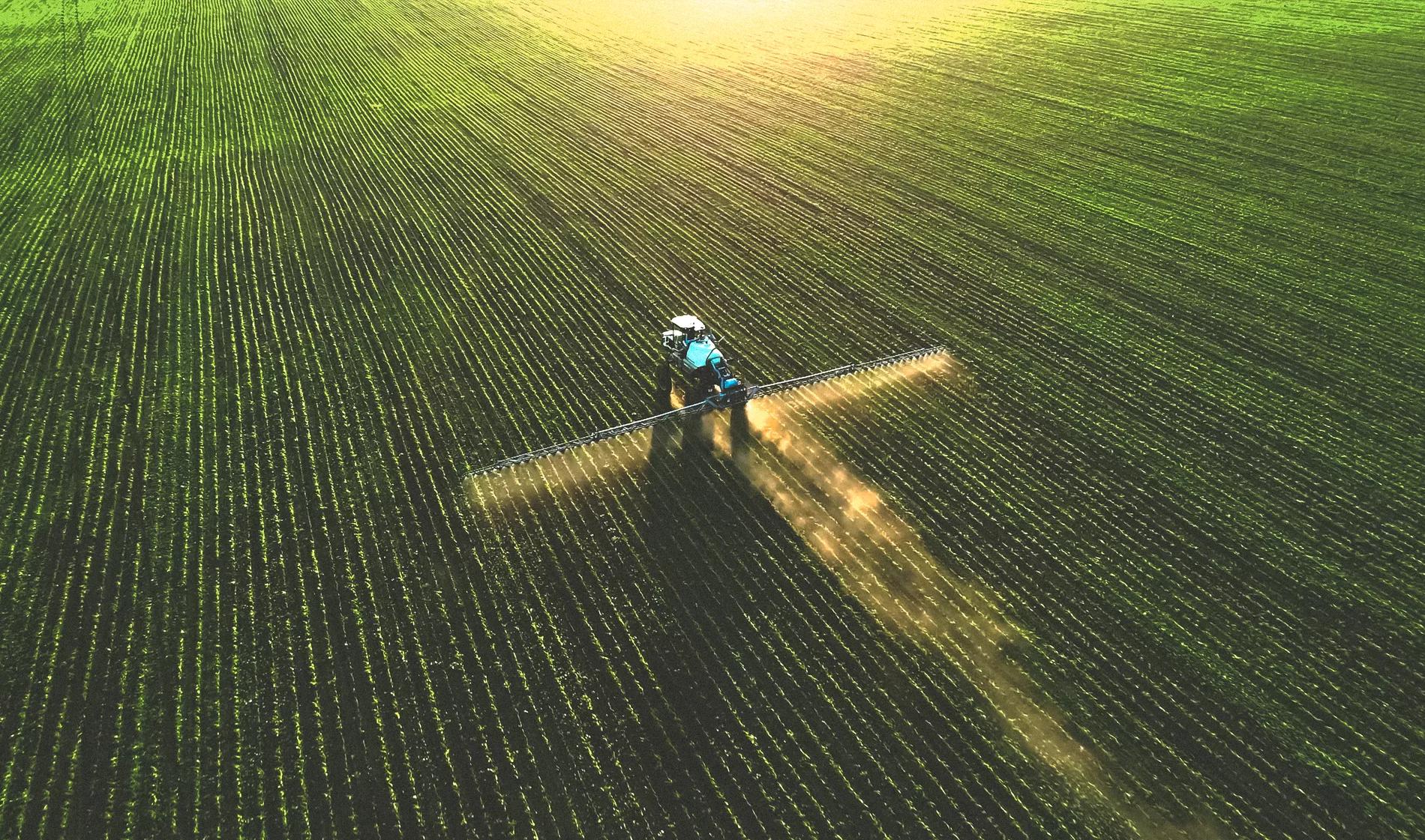 Tractor spraying fertilizer on a green field.
